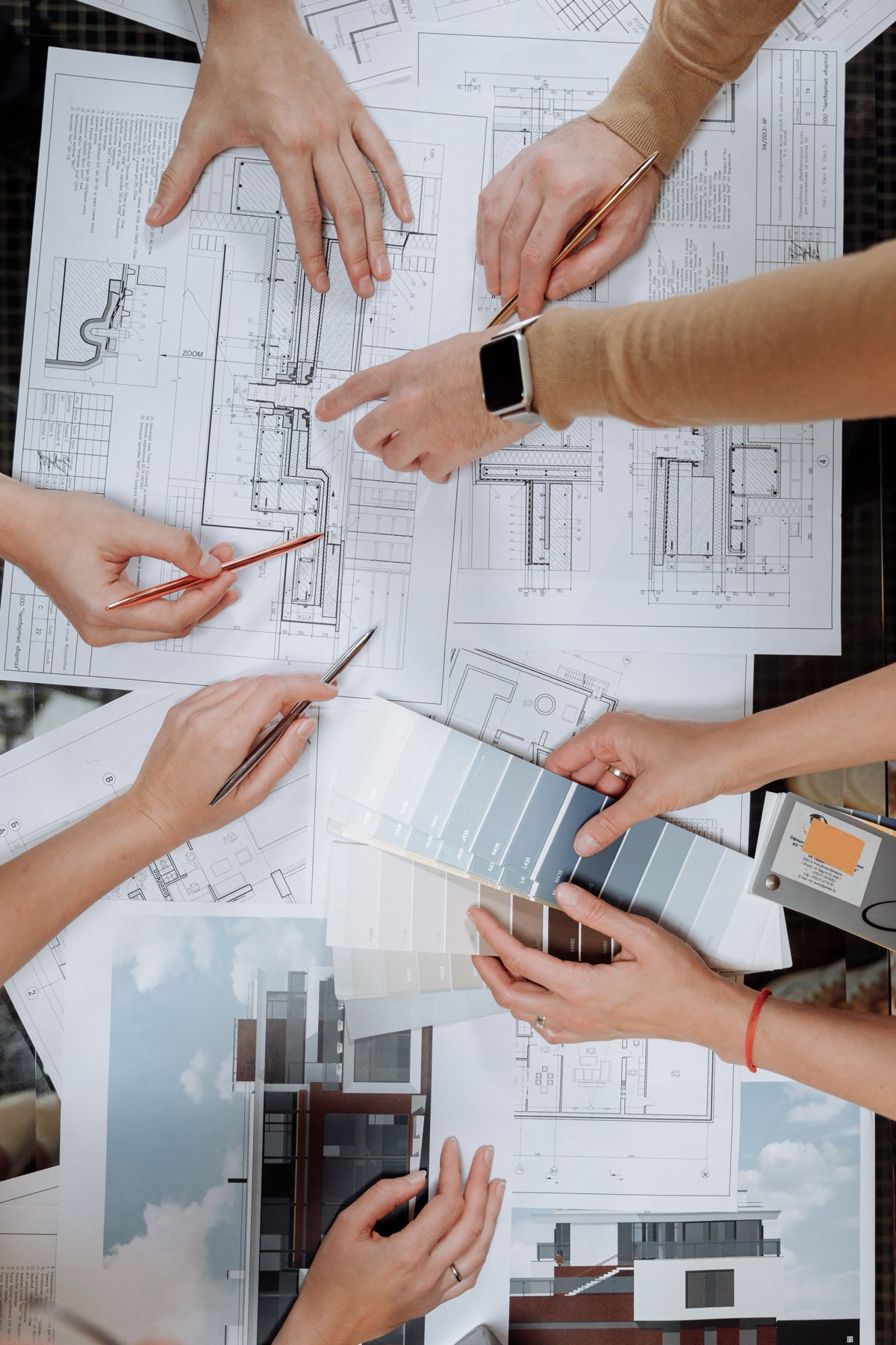 Drawings, plans and finish samples spread across a table during a design meeting