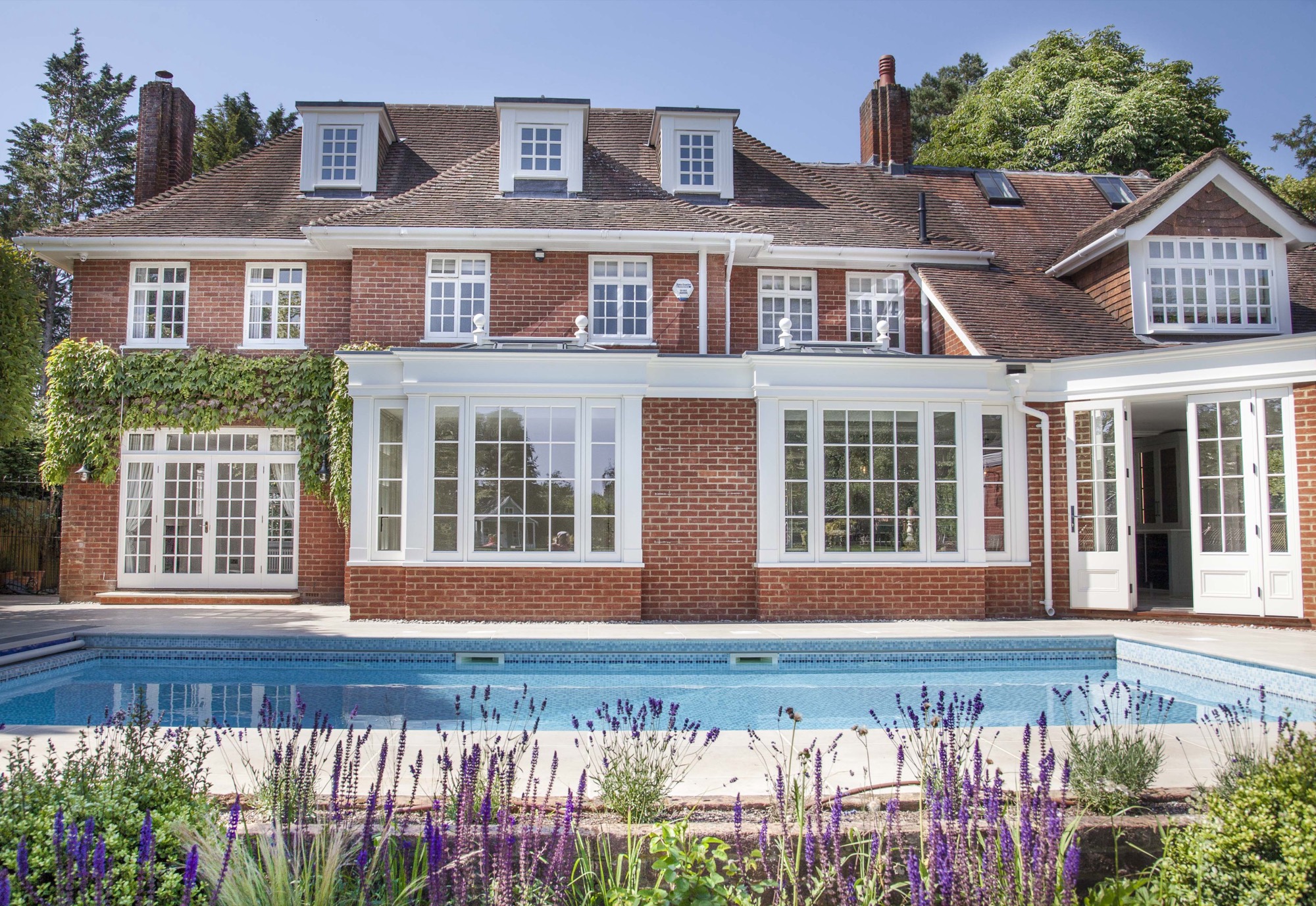 A completed brick house photographed across its pool terrace, with full-width glazing to the rear